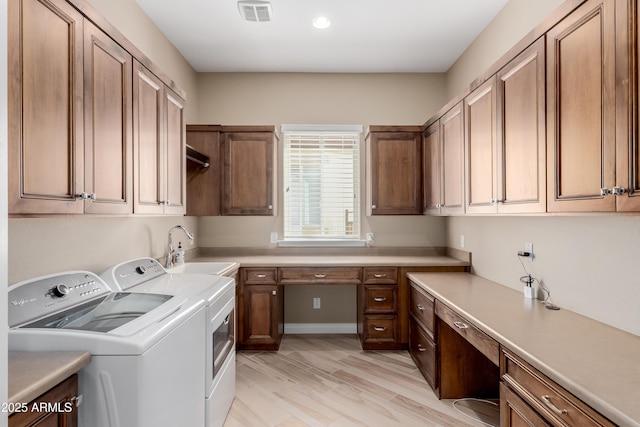 laundry room featuring washing machine and dryer, a sink, visible vents, light wood-style floors, and cabinet space