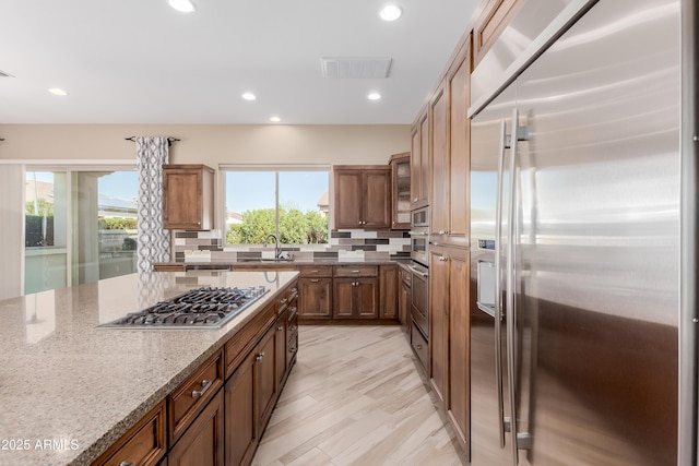 kitchen with tasteful backsplash, visible vents, light stone countertops, stainless steel appliances, and a sink