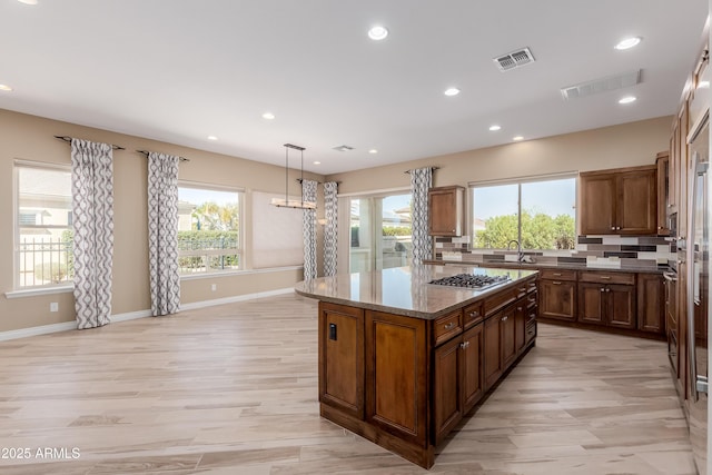 kitchen featuring a center island, visible vents, a healthy amount of sunlight, decorative backsplash, and stainless steel gas stovetop