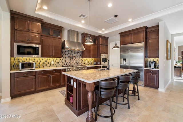 kitchen with visible vents, a raised ceiling, a sink, wall chimney exhaust hood, and built in appliances