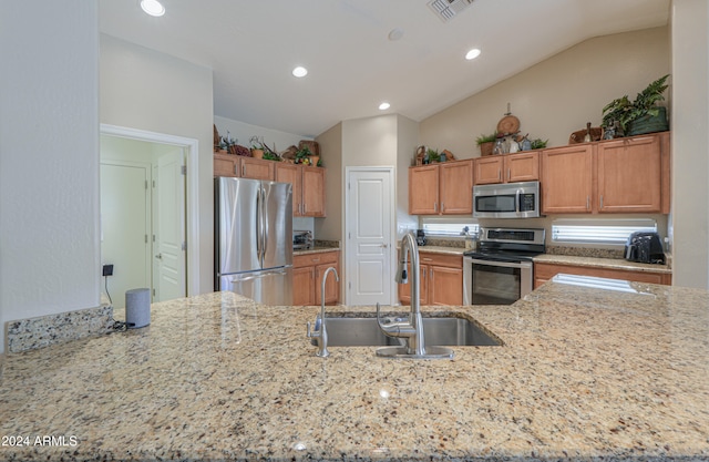 kitchen featuring light stone countertops, lofted ceiling, sink, and appliances with stainless steel finishes