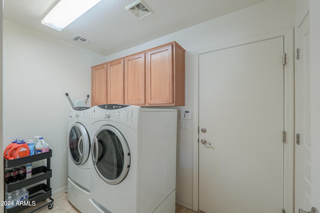 clothes washing area featuring washer and clothes dryer, light tile patterned floors, and cabinets