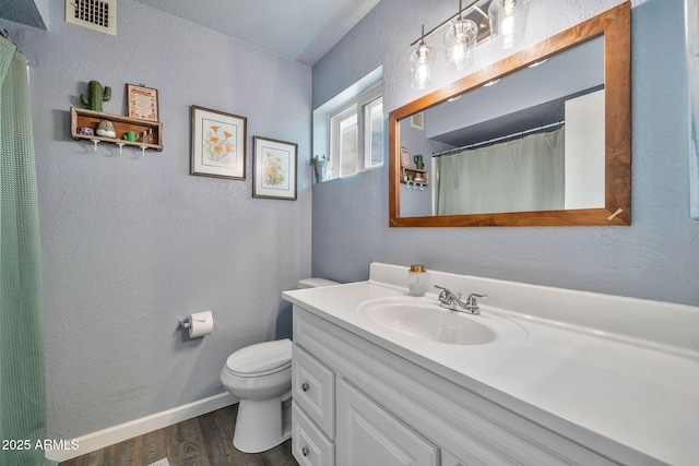 bathroom featuring vanity, wood finished floors, visible vents, toilet, and a textured wall