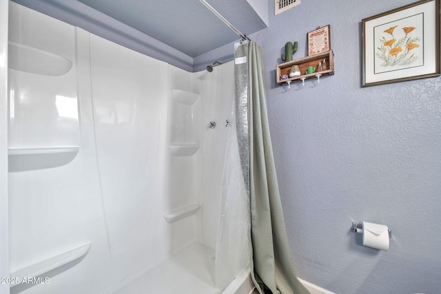 bathroom featuring a textured wall, visible vents, and a stall shower