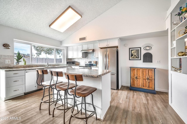 kitchen featuring visible vents, a kitchen island, stainless steel appliances, under cabinet range hood, and a kitchen breakfast bar