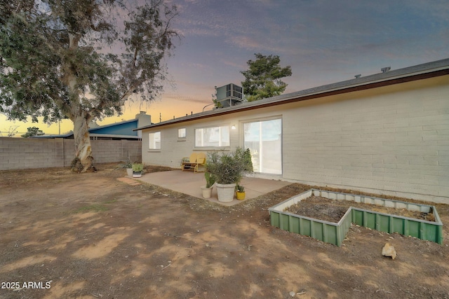 back of property at dusk featuring fence, a garden, brick siding, central AC unit, and a patio area