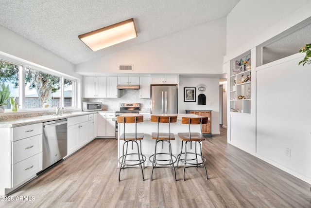 kitchen featuring visible vents, a kitchen island, lofted ceiling, a kitchen breakfast bar, and stainless steel appliances