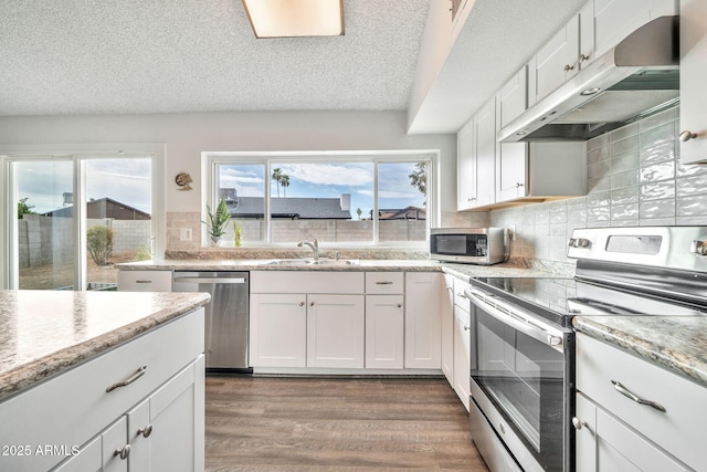 kitchen with under cabinet range hood, wood finished floors, white cabinets, stainless steel appliances, and a sink