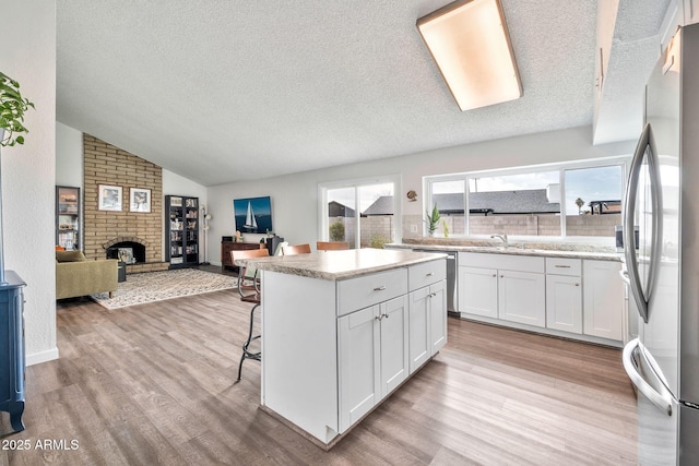 kitchen with light wood finished floors, vaulted ceiling, appliances with stainless steel finishes, white cabinetry, and a center island