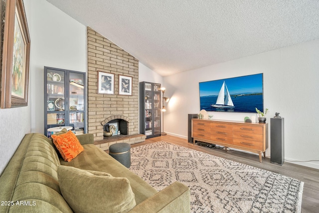 living area featuring wood finished floors, baseboards, lofted ceiling, a textured ceiling, and a brick fireplace