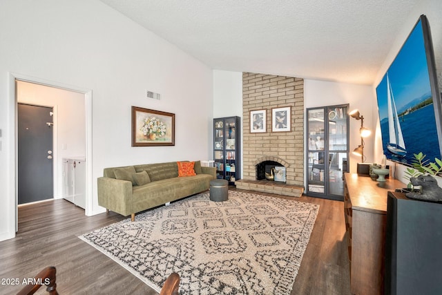 living area featuring visible vents, a brick fireplace, a textured ceiling, and wood finished floors