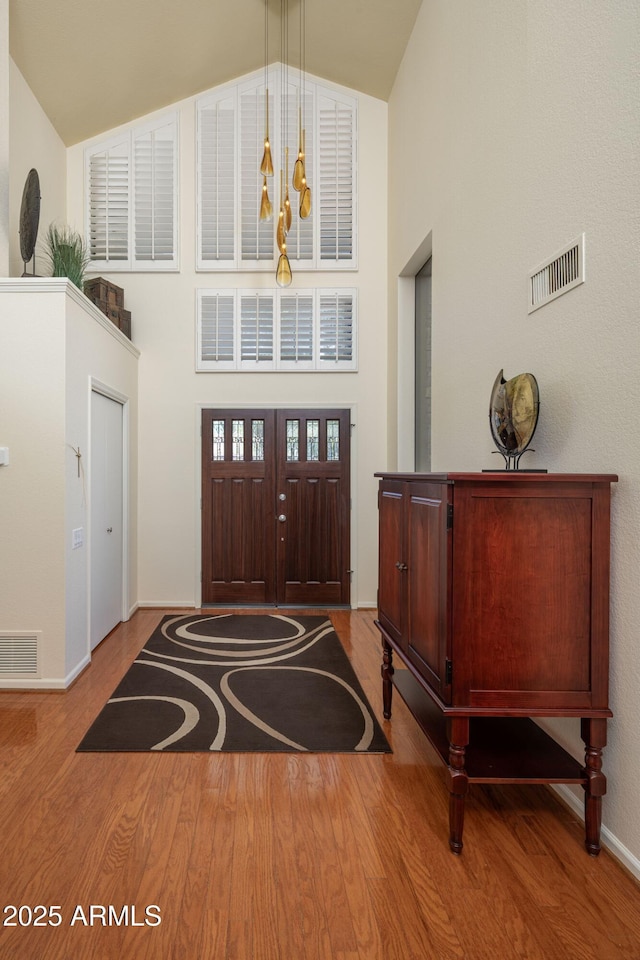 foyer entrance with high vaulted ceiling, wood finished floors, visible vents, and baseboards