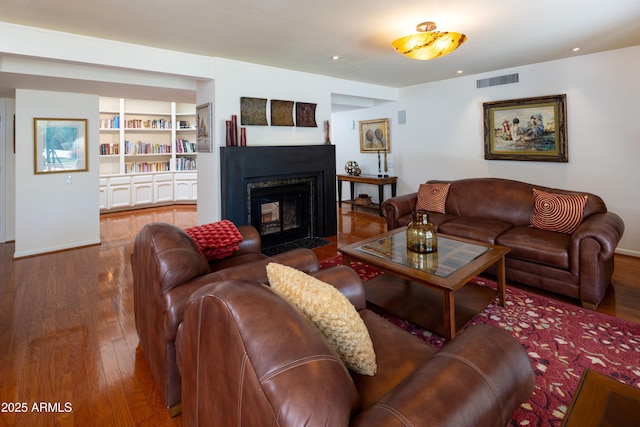 living area with built in shelves, recessed lighting, a fireplace with flush hearth, visible vents, and hardwood / wood-style floors