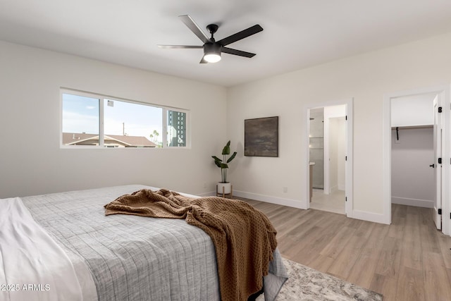 bedroom featuring ensuite bathroom, light wood-style flooring, baseboards, a ceiling fan, and a spacious closet