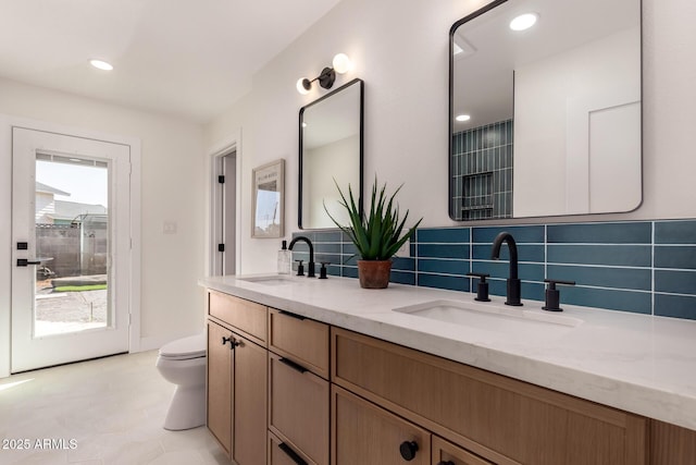 full bathroom featuring double vanity, a sink, toilet, and tasteful backsplash