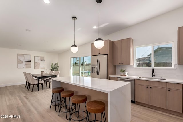 kitchen featuring a breakfast bar, a kitchen island, appliances with stainless steel finishes, a sink, and backsplash