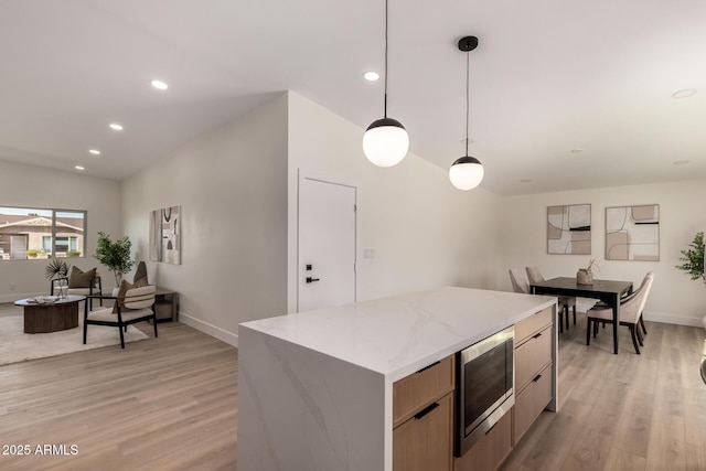 kitchen featuring hanging light fixtures, stainless steel microwave, light wood-style floors, and a center island