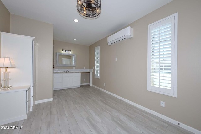 unfurnished living room with light wood-type flooring, sink, and a wall unit AC