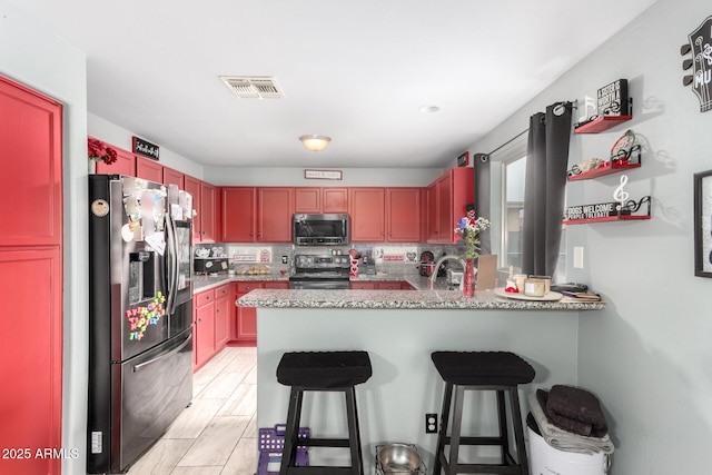 kitchen featuring visible vents, a breakfast bar, a peninsula, stainless steel appliances, and a sink