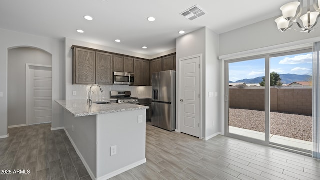 kitchen featuring a sink, visible vents, a peninsula, dark brown cabinets, and appliances with stainless steel finishes