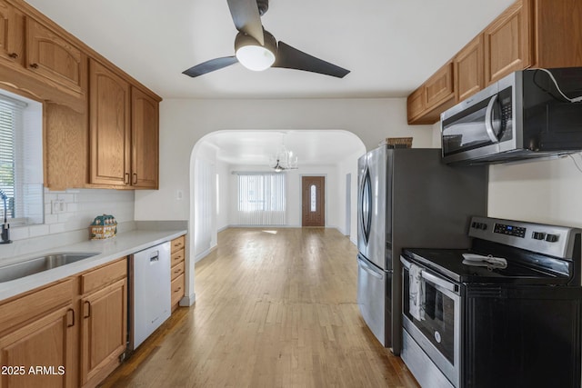 kitchen with appliances with stainless steel finishes, hanging light fixtures, decorative backsplash, light hardwood / wood-style floors, and sink