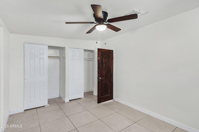 unfurnished bedroom with light tile patterned floors, ceiling fan, and two closets