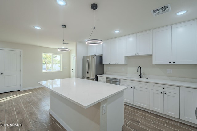 kitchen with appliances with stainless steel finishes, dark hardwood / wood-style flooring, sink, white cabinets, and hanging light fixtures