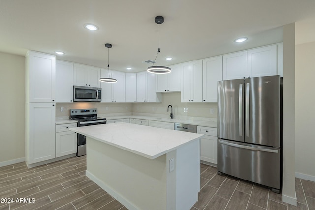 kitchen with a center island, hanging light fixtures, stainless steel appliances, light stone counters, and white cabinets