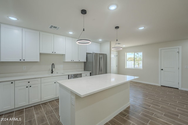 kitchen with white cabinetry, stainless steel appliances, pendant lighting, wood-type flooring, and a kitchen island