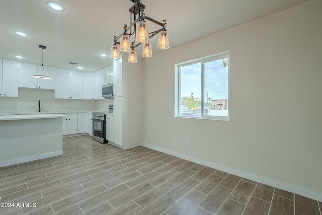 kitchen with appliances with stainless steel finishes, sink, pendant lighting, an inviting chandelier, and white cabinets