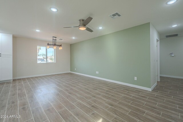 empty room featuring ceiling fan with notable chandelier and light hardwood / wood-style floors