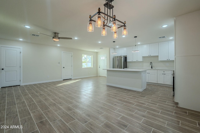 kitchen featuring white cabinetry, sink, hanging light fixtures, light hardwood / wood-style flooring, and stainless steel fridge