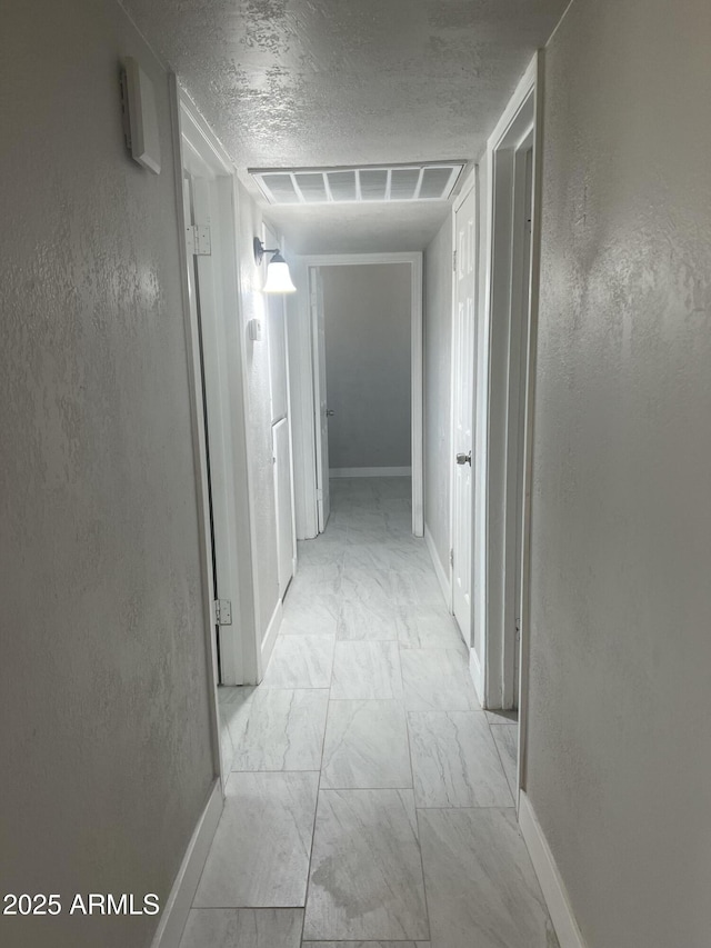 corridor featuring visible vents, marble finish floor, a textured ceiling, and a textured wall