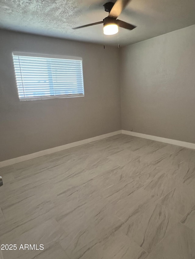 spare room featuring ceiling fan, a textured ceiling, and baseboards