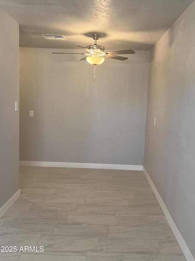 empty room featuring a textured ceiling, baseboards, visible vents, and ceiling fan