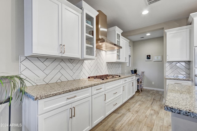 kitchen with light stone countertops, wall chimney exhaust hood, stainless steel gas stovetop, decorative backsplash, and white cabinets