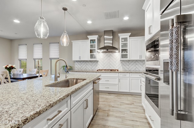 kitchen featuring sink, stainless steel appliances, wall chimney range hood, decorative backsplash, and white cabinets