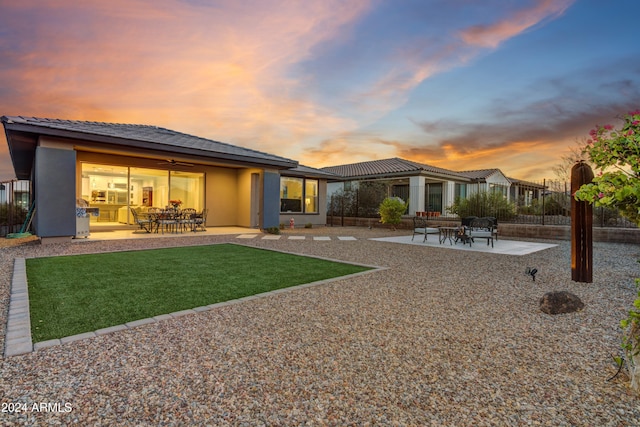 back house at dusk featuring a lawn, ceiling fan, and a patio