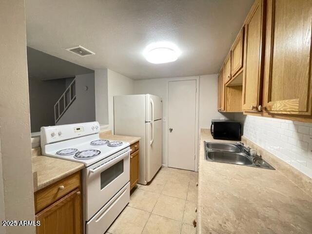 kitchen featuring white appliances, visible vents, brown cabinetry, and a sink