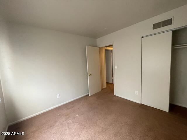 unfurnished bedroom featuring carpet floors, baseboards, a closet, and visible vents