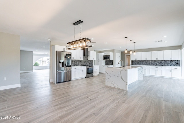 kitchen featuring white cabinets, light hardwood / wood-style flooring, stainless steel appliances, pendant lighting, and a kitchen island with sink