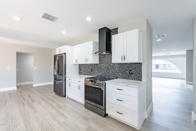 kitchen with wall chimney range hood, white cabinets, stainless steel appliances, and light hardwood / wood-style flooring