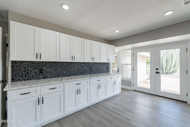 kitchen featuring white cabinets, french doors, light wood-type flooring, light stone counters, and decorative backsplash