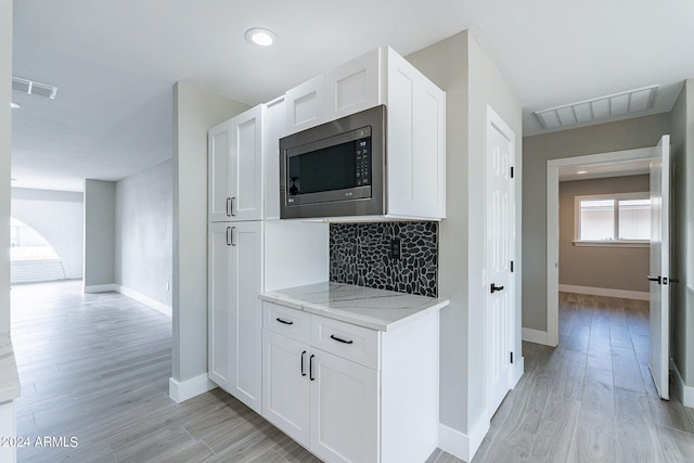 kitchen with light wood-type flooring, stainless steel microwave, white cabinets, and light stone countertops