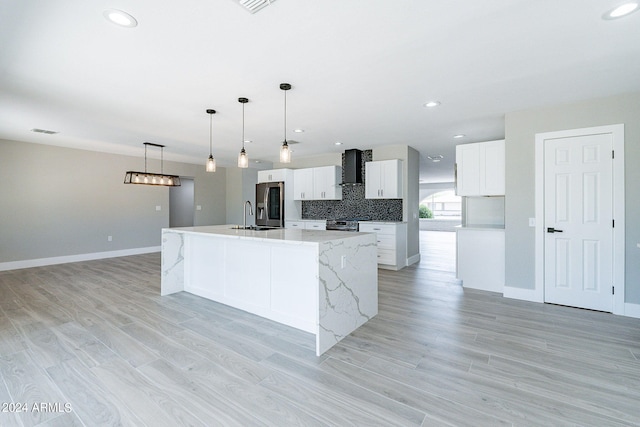 kitchen featuring a spacious island, pendant lighting, light hardwood / wood-style floors, white cabinetry, and wall chimney range hood