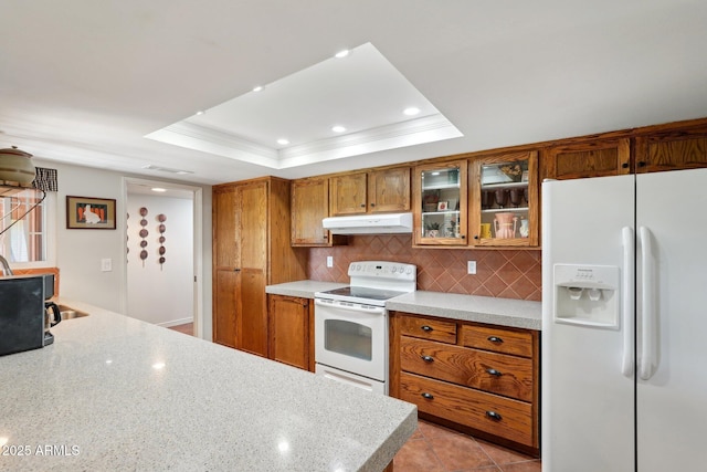 kitchen with crown molding, light tile patterned floors, a tray ceiling, white appliances, and backsplash