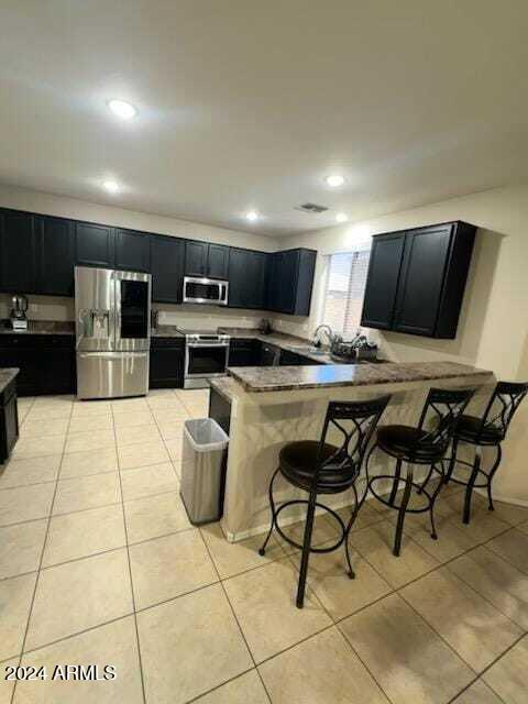 kitchen featuring dark stone counters, a kitchen breakfast bar, light tile patterned floors, kitchen peninsula, and stainless steel appliances