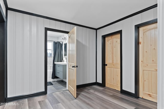 unfurnished bedroom featuring ensuite bath, crown molding, wood finished floors, and baseboards