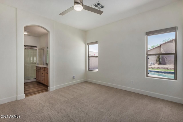 unfurnished bedroom featuring ensuite bathroom, dark carpet, and ceiling fan