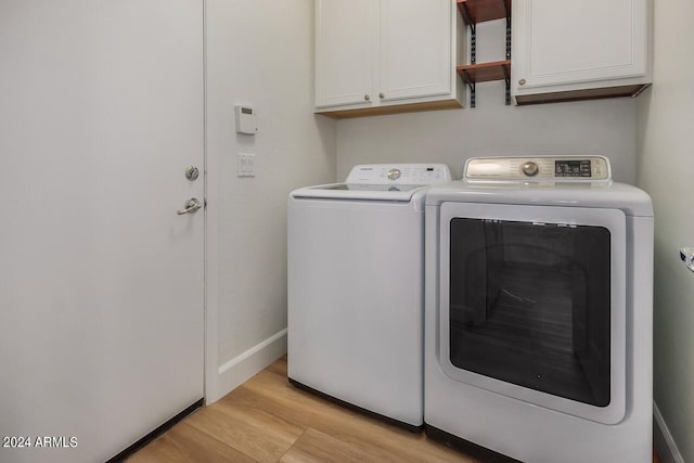 laundry area with washing machine and clothes dryer, light hardwood / wood-style floors, and cabinets